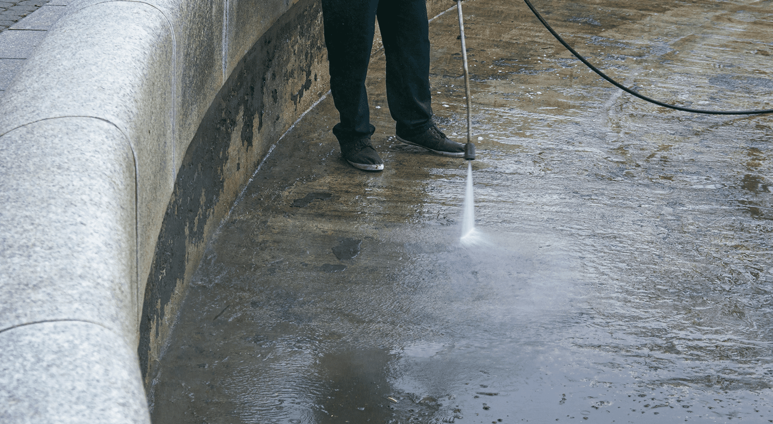 Person pressure washing a concrete surface.